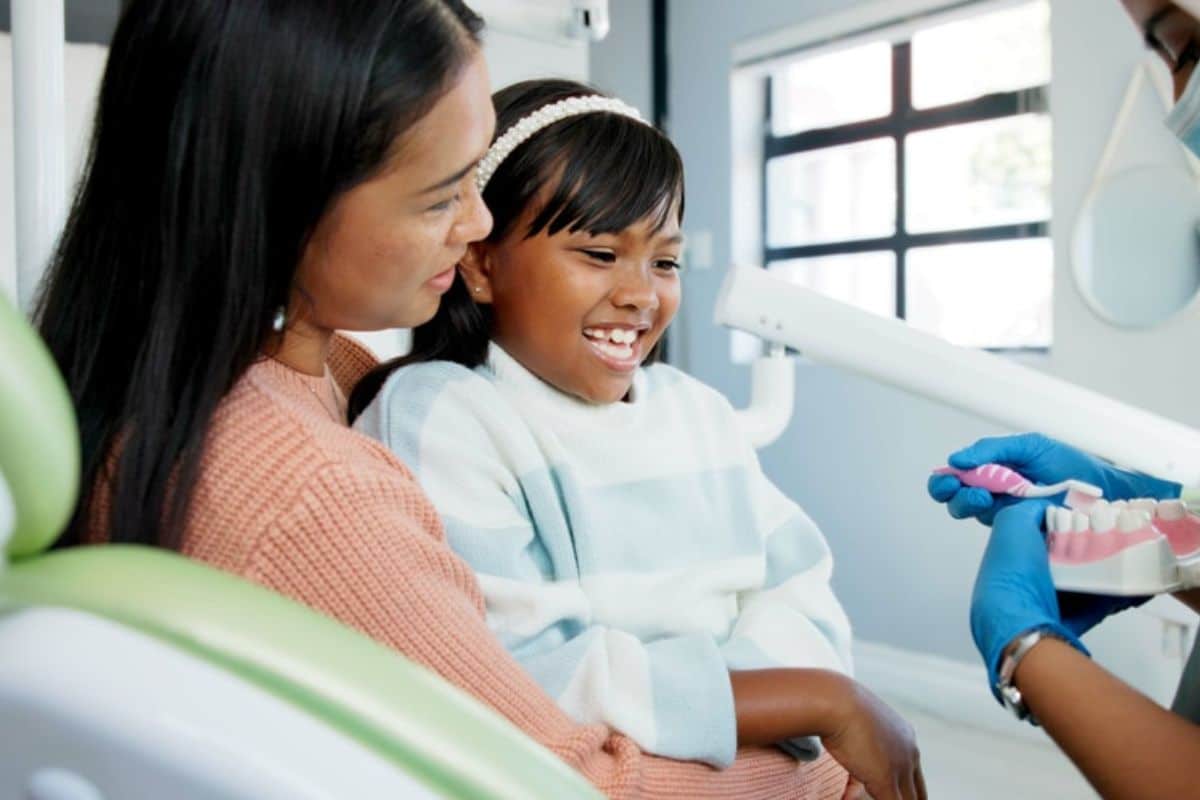 dentist showing how to clean teeth to the kid sitting with her mother
