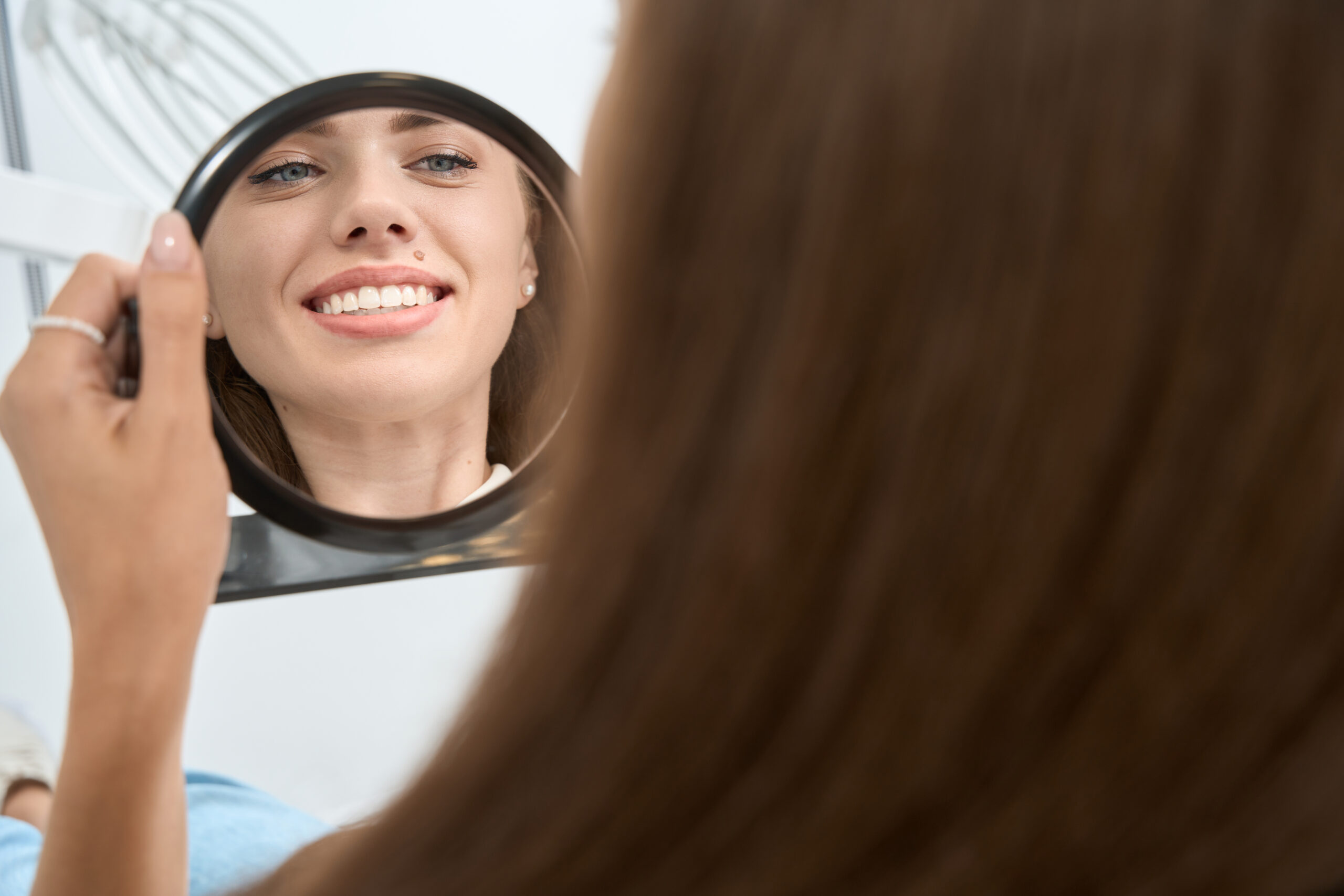 Patient smiling and examining her teeth in a hand mirror before cosmetic dental treatment