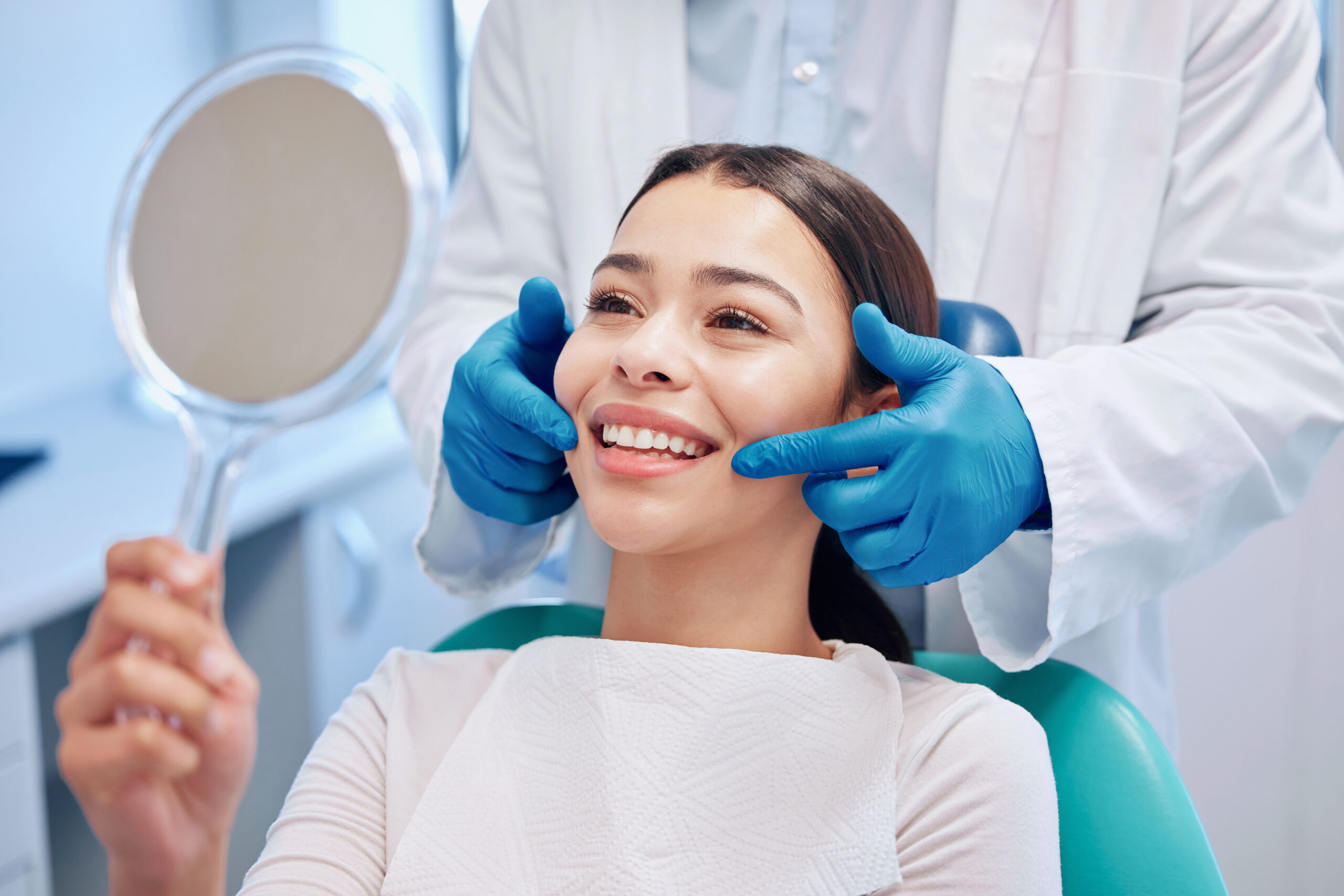 Woman smiling in a dental chair while her dentist gently examines her smile before a cosmetic procedure