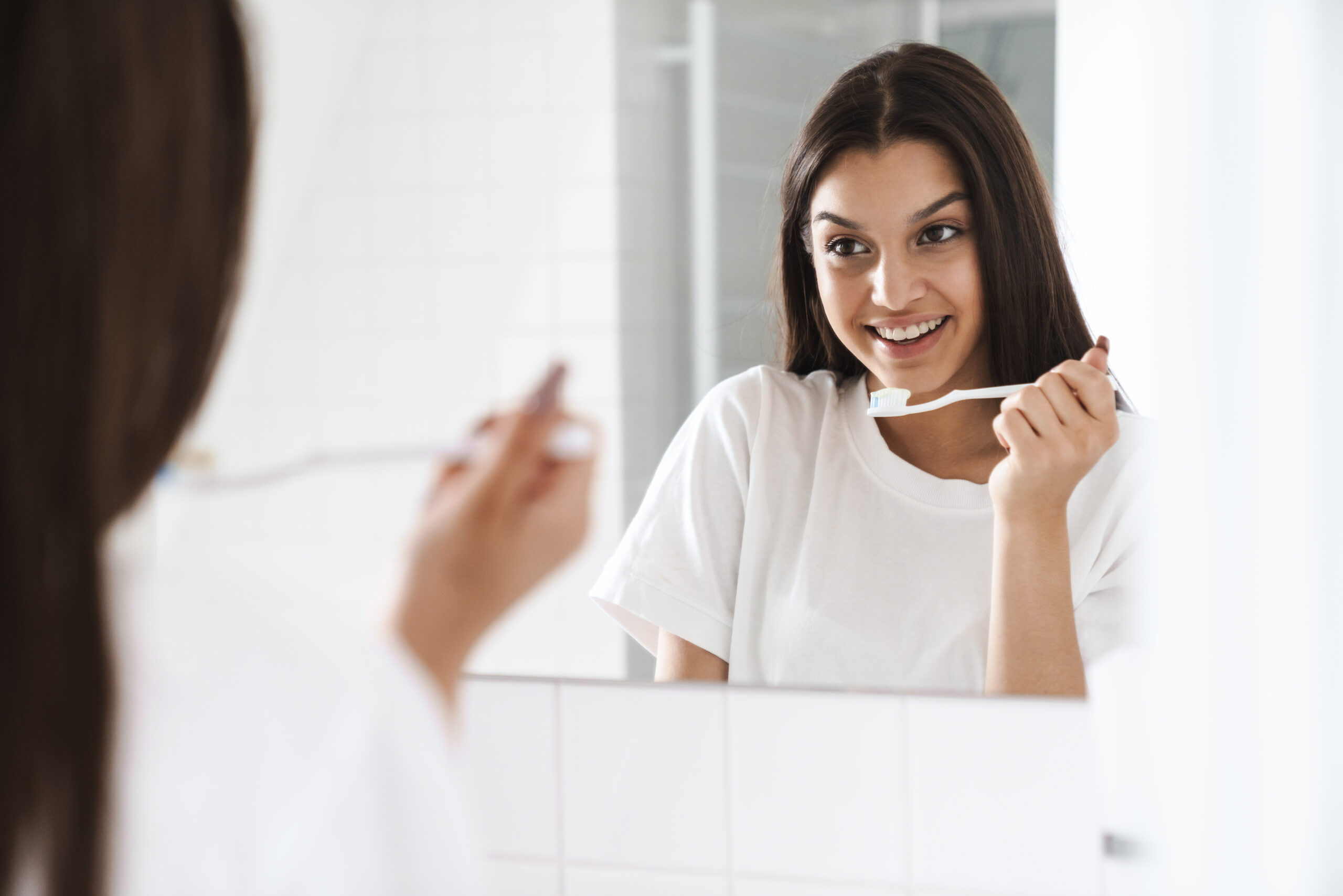 Woman brushing her teeth in front of a mirror, demonstrating a healthy daily oral care routine