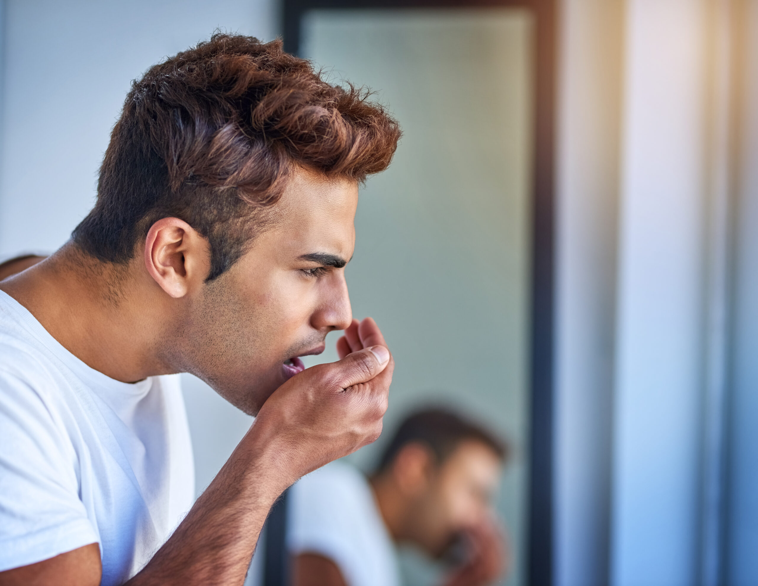 Man checking his breath in the mirror, concerned about persistent bad breath despite daily brushing